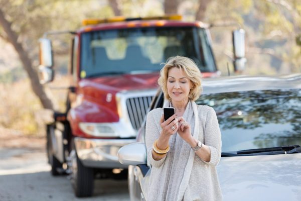 Senior woman with smart phone at roadside with car breakdown